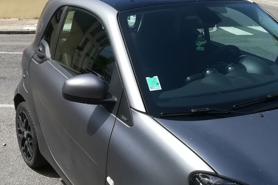 Vignette auto assurance collée sur un pare-brise d'un véhicule garé dans une rue.